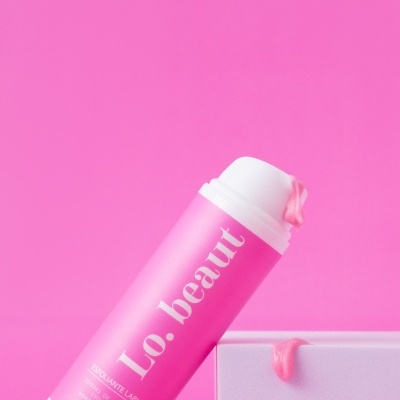 Esfoliante labial em embalagem rosa com creme rosa escorrendo sobre caixa branca em fundo rosa