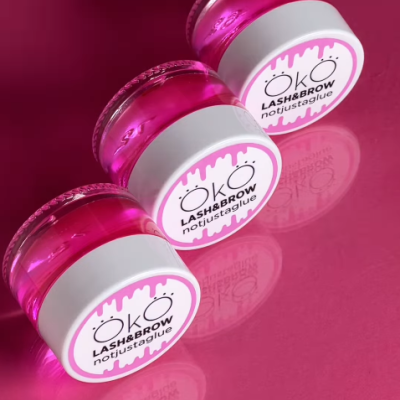 Três frascos de cola para pestanas e sobrancelhas ÖKO com líquido rosa e tampa branca em fundo rosa