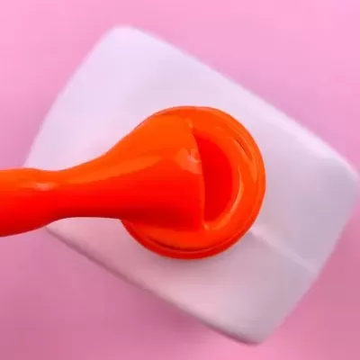 Pincel de verniz de unhas com tinta laranja em fundo rosa