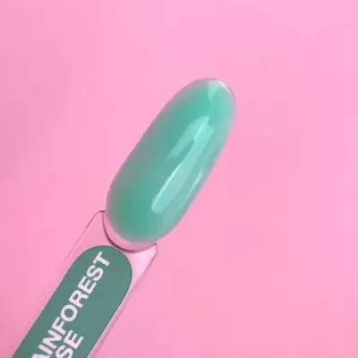 Amostra de verniz para unhas verde esmeralda com rótulo RAINFOREST BASE sobre fundo rosa