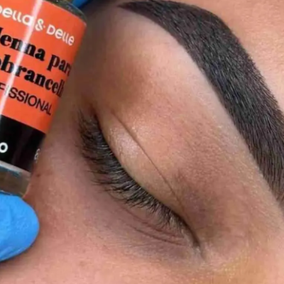 Frasco de henna para sobrancelhas com texto PRETO INTENSO junto a sobrancelha escura e mão com luva azul