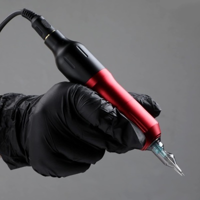 Máquina de tatuagem metálica vermelha e preta sendo segurada por mão com luva preta