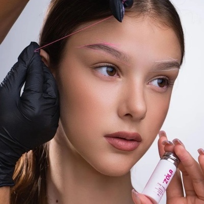 Mulher com sobrancelhas marcadas com fio rosado e branca segurando frasco ZOLA