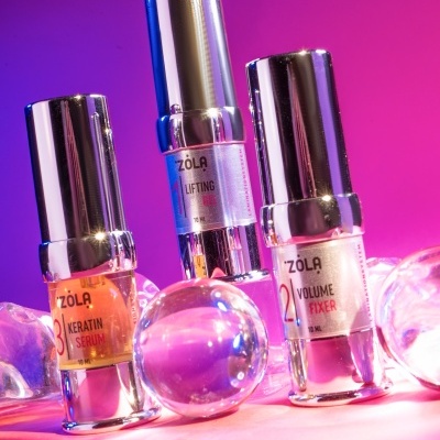 Três frascos de cosméticos ZOLA com tampas prateadas em ambiente rosa e roxo com esferas de vidro