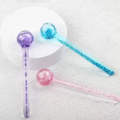 Três bastões de massagem transparentes com glitter azul, rosa e roxo em superfície branca