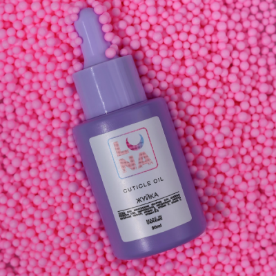 Frasco roxo de óleo para cutículas com conta-gotas sobre bolinhas rosas