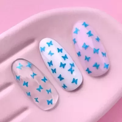 Três unhas postiças com padrões de borboletas azuis sobre bandeja rosa claro