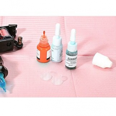 Frascos de tinta para tatuagem em superfície rosa com acessórios.