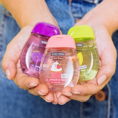 Três frascos pequenos de gel desinfetante para as mãos com tampas coloridas nas mãos de uma pessoa.