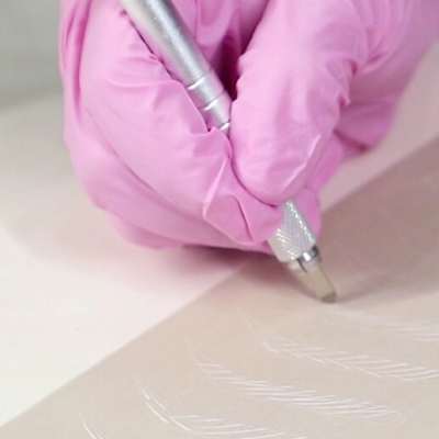 Mão com luva rosa usando ferramenta de gravação num papel bege