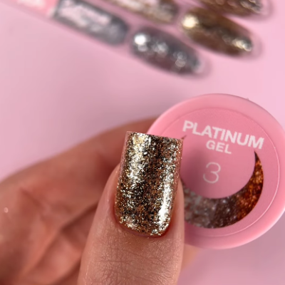 Frasco rosa de gel de unha com rótulo e unha com brilho dourado em destaque.