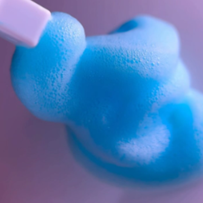 Espuma azul espessa sendo espalhada por espátula branca sobre superfície lilás