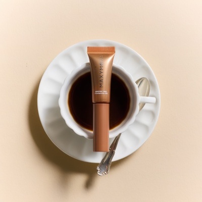Tubo de gel para sobrancelhas castanho sobre chávena branca de café.