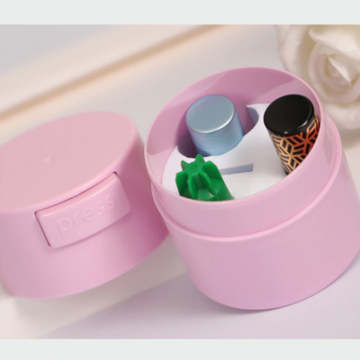 Caixa rosa redonda com tampa, contendo três pequenos frascos coloridos