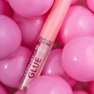 Cola para pestanas ZOLA Lash Lift Glue com tampa rosa entre bolas plásticas cor de rosa