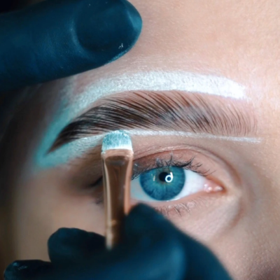 pincel aplicando produto branco em sobrancelha com mão de luva preta