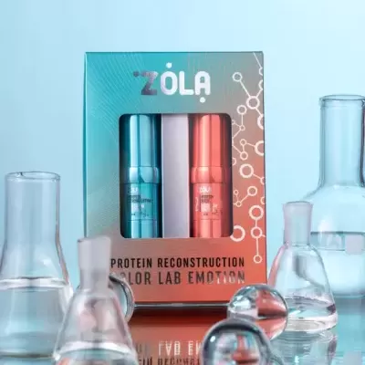 Caixa ZÓLA com dois frascos metálicos azul e rosa, rodeada por frascos de ensaio transparentes