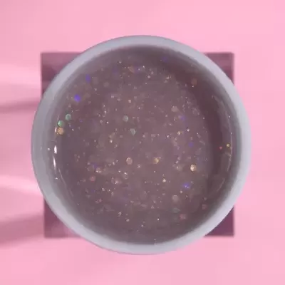 Recipiente branco com gel glitter multicolorido sobre fundo rosa claro.