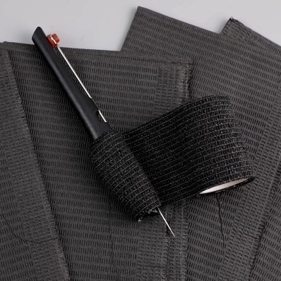 Fitas adesivas pretas e ferramenta preta sobre tecido preto com padrão texturizado.