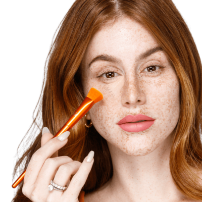 Mulher ruiva a aplicar maquilhagem no rosto com pincel laranja e cerdas amarelas