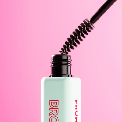 Máscara de sobrancelhas branca com aplicador preto contra fundo rosa