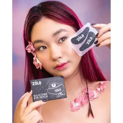 Pessoa com cabelo rosa segurando embalagem preta ZOLA Silicone Eye Patch e cartão com patches pretas