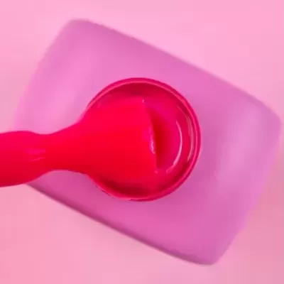 Frasco aberto de verniz de unha rosa com pincel sobre fundo rosa.