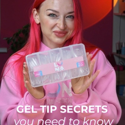 Mulher com cabelo rosa segura caixa transparente de gel tips na mesa com fundo vermelho e luz amarela