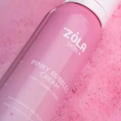 Frasco rosa de creme de limpeza espumante ZÔLA SKIN sobre espuma rosa