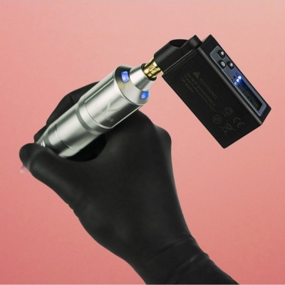 Mão com luva preta segurando aparelho metálico conectado a dispositivo eletrônico preto com luzes LED