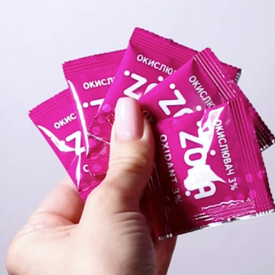 Pacotes cor-de-rosa de oxidante 3% em mão com unhas rosa claro