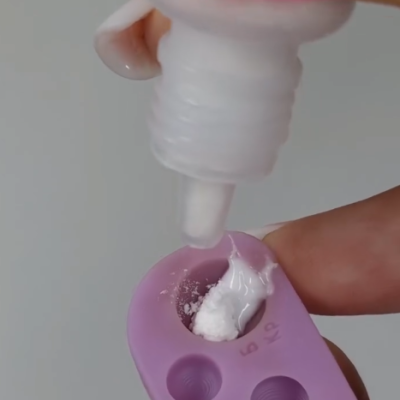 Bisnaga a despejar creme branco em molde de silicone lilás com marcações 5 e KP