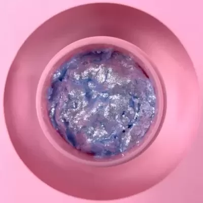 Frasco rosa com creme azul e prateado visto de cima, fundo rosa