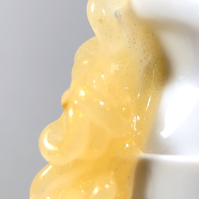 Gel dourado translúcido com partículas brilhantes numa superfície branca curva