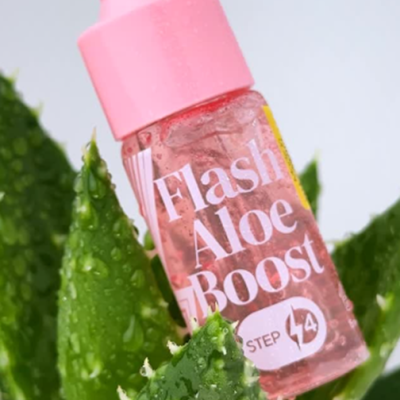 Frasco rosa de Flash Aloe Boost sobre folhas de aloe vera molhadas