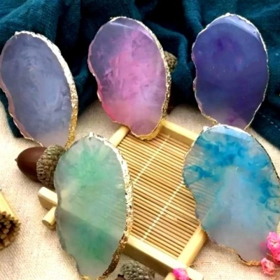 Cinco bases de pedra de ágata colorida com bordas douradas dispostas sobre superfície neutra