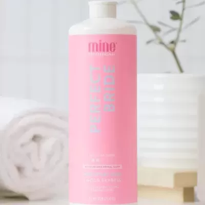 garrafa de produto rosa e branco Mine Professional Perfect Bride com toalha e planta ao fundo