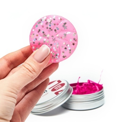 Disco redondo rosa com estrelas prateadas segurado por mão ao lado de embalagem metálica aberta