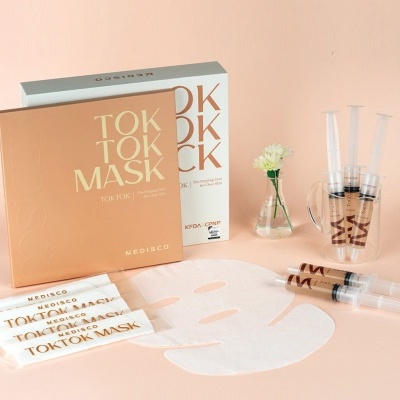 Pacotes de TOKTOK MASK da MEDISCO com máscara facial branca e seringas em fundo pêssego