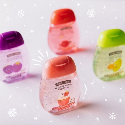 Quatro frascos pequenos de gel limpador de mãos com tampas coloridas e rótulos com frutas.