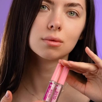Mulher segura dois frascos transparentes de cola para pestanas com tampa rosa e texto LASH LIFT GLUE.