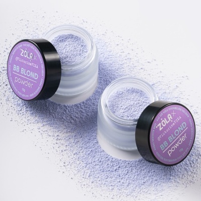 Dois frascos de vidro com tampa preta e etiquetas lilás com pó de cosmético lilás disperso no fundo branco.