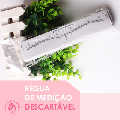 Régua de medição descartável branca com marcações pretas embalada em plástico sobre fundo branco e folhas verdes artificiais