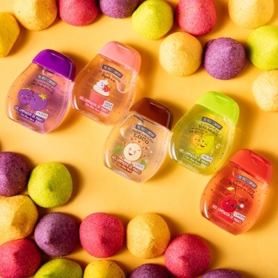 Cinco frascos pequenos de gel desinfetante coloridos rodeados por bolas coloridas de espuma