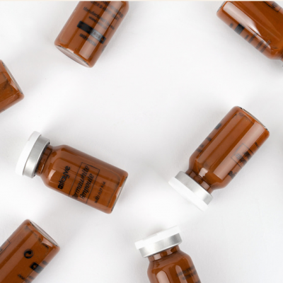 Frascos pequenos de vidro castanho com tampas brancas e texto impresso preto, dispostos em superfície branca