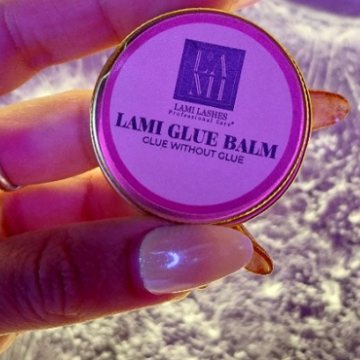 Frasco pequeno redondo de LAMI GLUE BALM com tampa roxa e dourada segurado por mão com unhas compridas