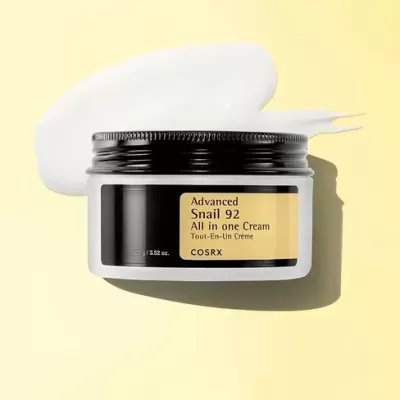 Frasco de creme COSRX Advanced Snail 92 com rótulo amarelo e tampa preta sobre fundo amarelo