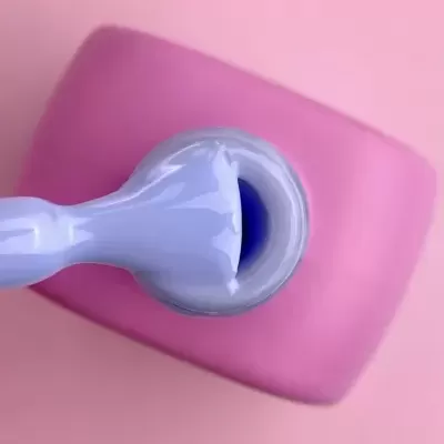 Frasco aberto de verniz lilás com pincel, sobre superfície rosa.