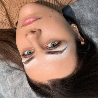 Rosto de mulher com olhos verdes e sobrancelhas delineadas com branco