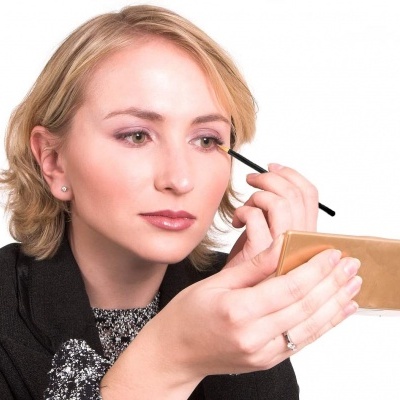 Mulher loira aplica maquilhagem nos olhos com pincel e espelho dourado